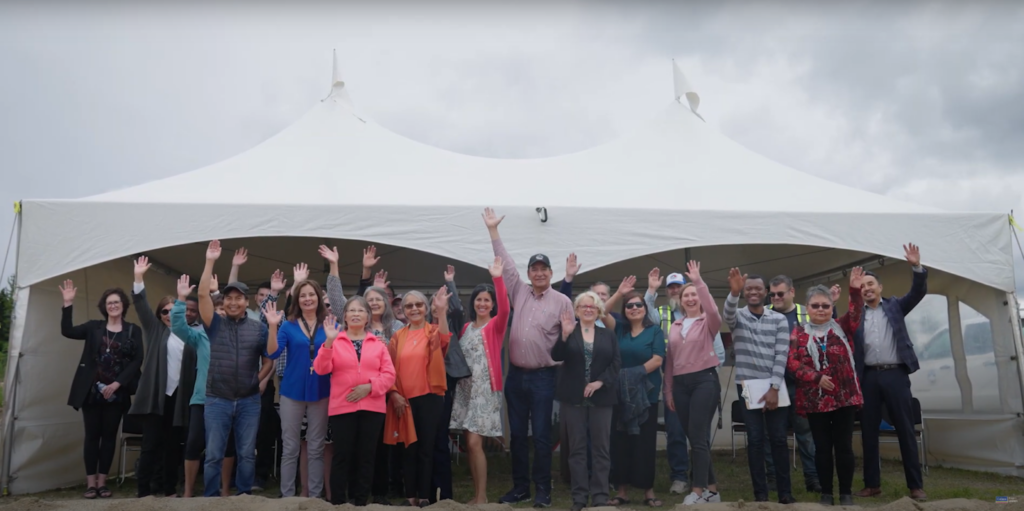 People smiling and waving outside in front of a tent
