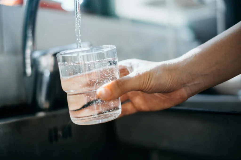Woman holding glass under tap, filling it with water