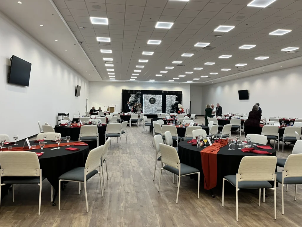 inside of a room with multiple round tables that have black table cloths on them with a red runner in the middle
