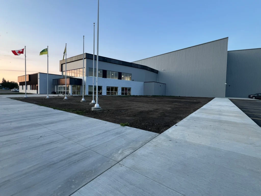 Exterior of a building with the Canadian Flag, Saskatchewan flag are flying high on a flagpole on the left of the photo